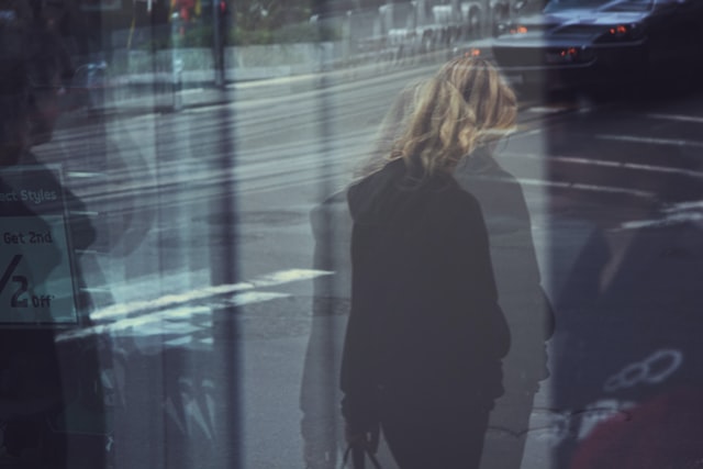 Woman walking on the street wearing black jacket, shot through several windows, blurred